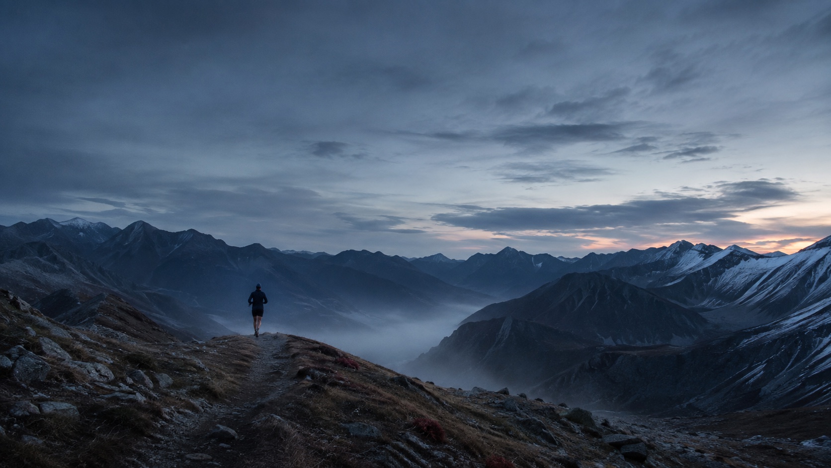 An anonymous trail runner moving through a mountain landscape before sunrise